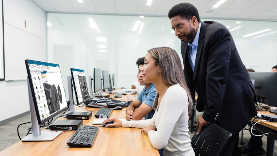 Engineering students and their professor in a computer lab using Designcenter X NX Academic Edition. A female student is using modeling CAD features, and a male student is doing CAM.
