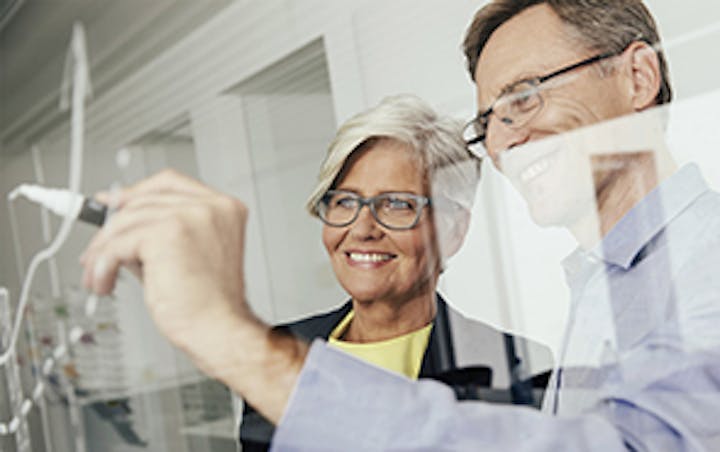 Zwei Personen zeichnen lächelnd mit weißem Marker auf einem Glas-Bildschirm