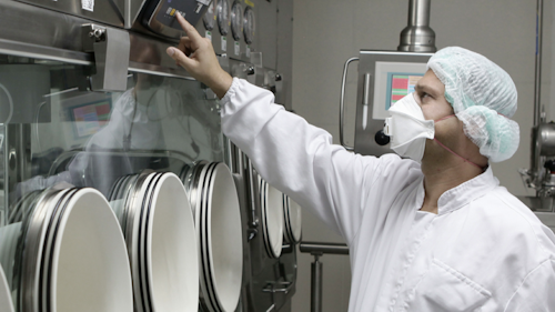 在医疗器械制造工厂中，一名身着个人防护装备 (PPE)、带着面罩的白人男性正在按下机器上的按钮