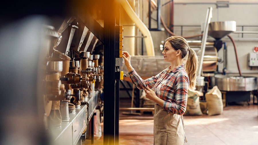 A female coffee factory worker starting machine for coffee grinding.