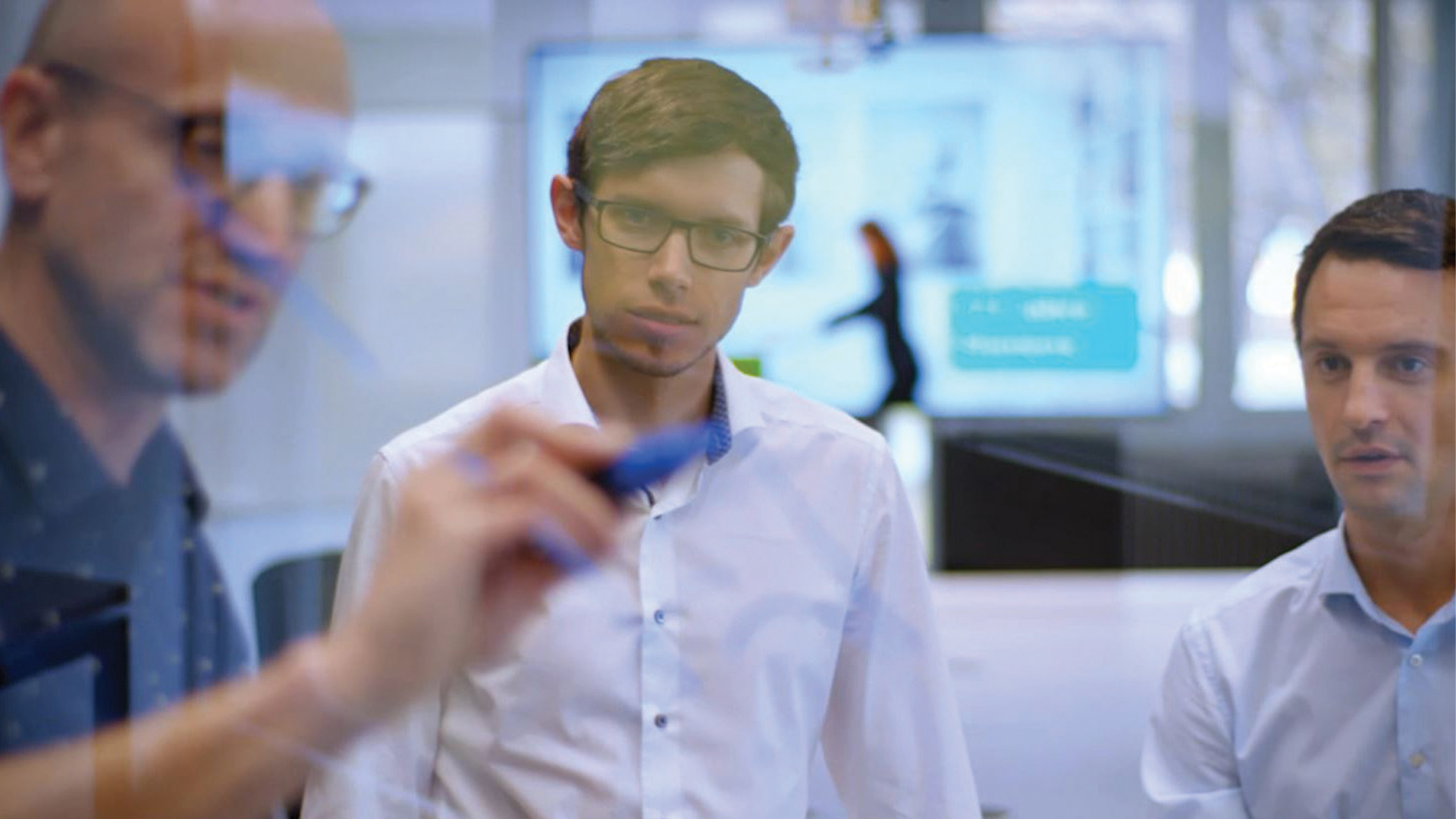 Engineers collaborate at a glass board to plan out a manufacturing production process.