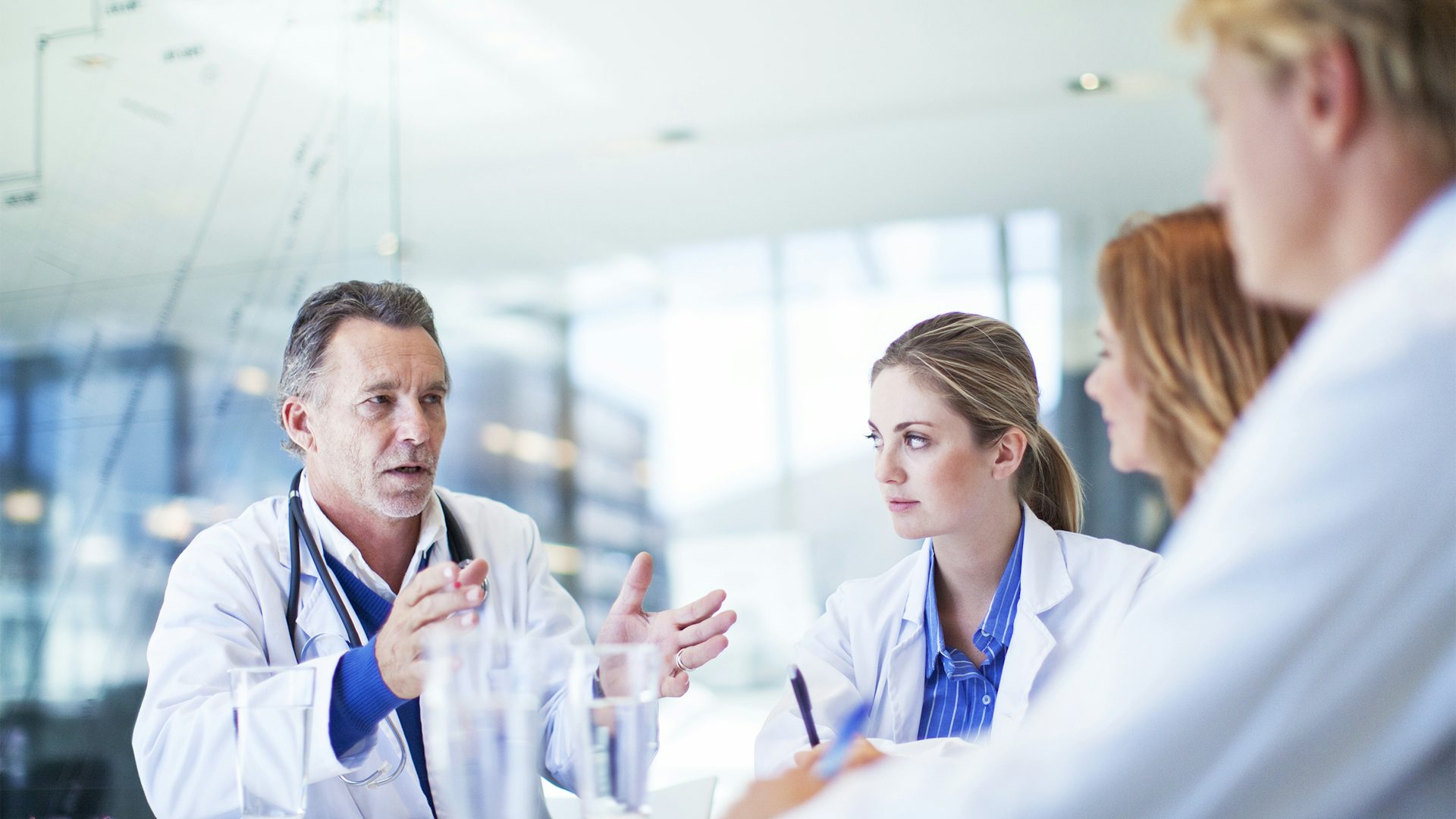 A male doctor talks to three colleagues, two of which are out of focus.