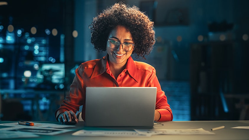 オフィスで夜に微笑みながらノートパソコンを見ている女性。