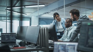 A group of diverse engineers sitting around a computer and discussing.