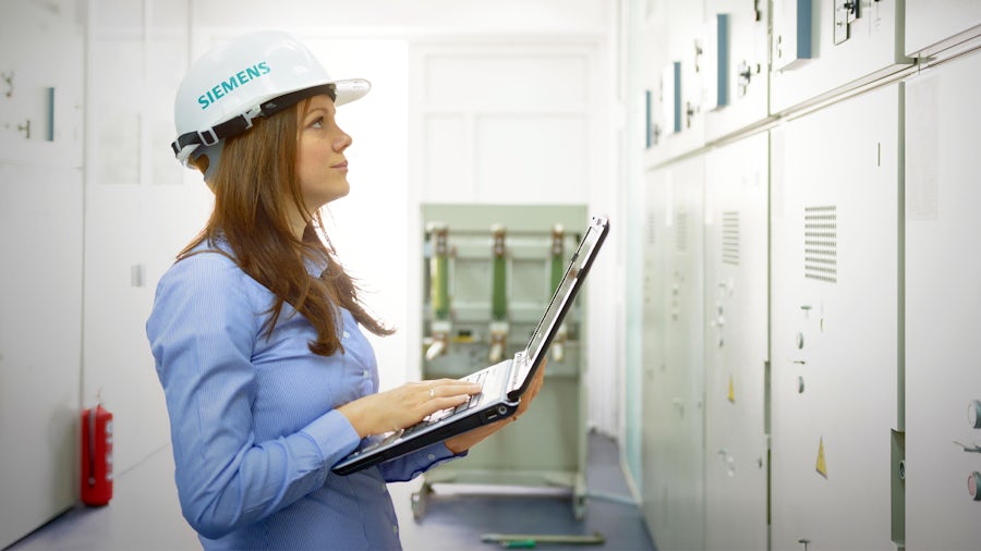 A service engineer looks at her laptop and industrial machinery.
