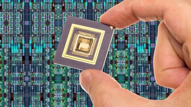 Pacakaged IC held between two fingers, in front of an IC layout