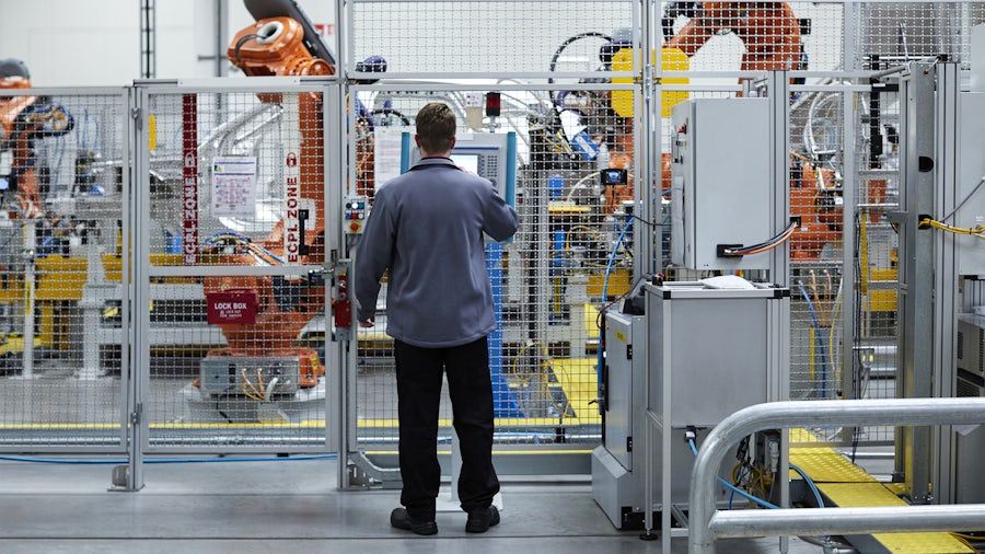 An industrial machine operator works at a control panel.