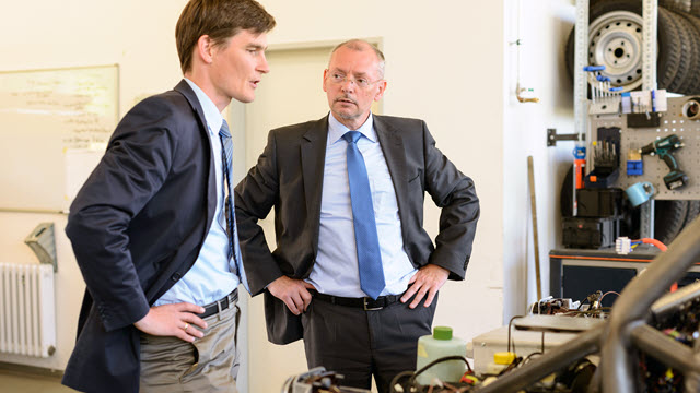 Two men in suits with hands on hips are conversing in a tire shop.