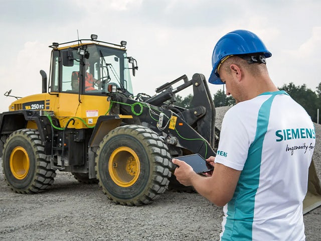 A Siemens engineer stands beside a JCB tractor, performing durability testing.