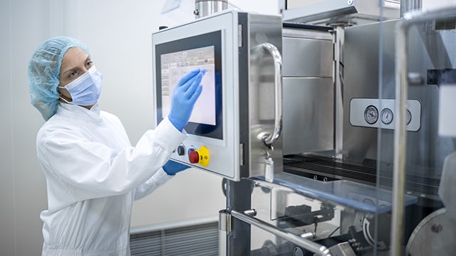 A person in scrubs and gloves monitoring Insight Hub Solutions on a computer screen in a lab.