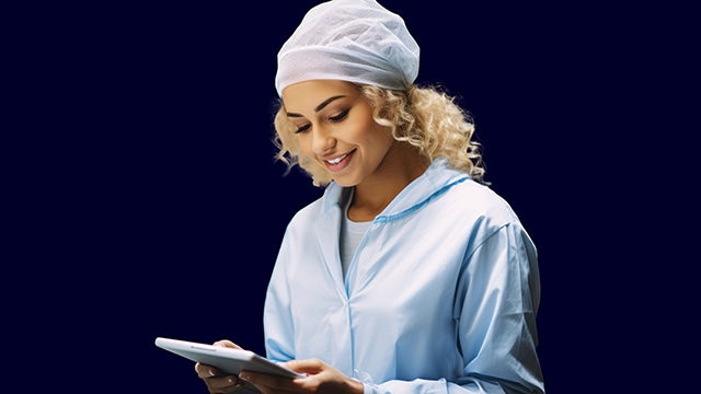 Woman wearing scrubs holding a tablet and smiling.