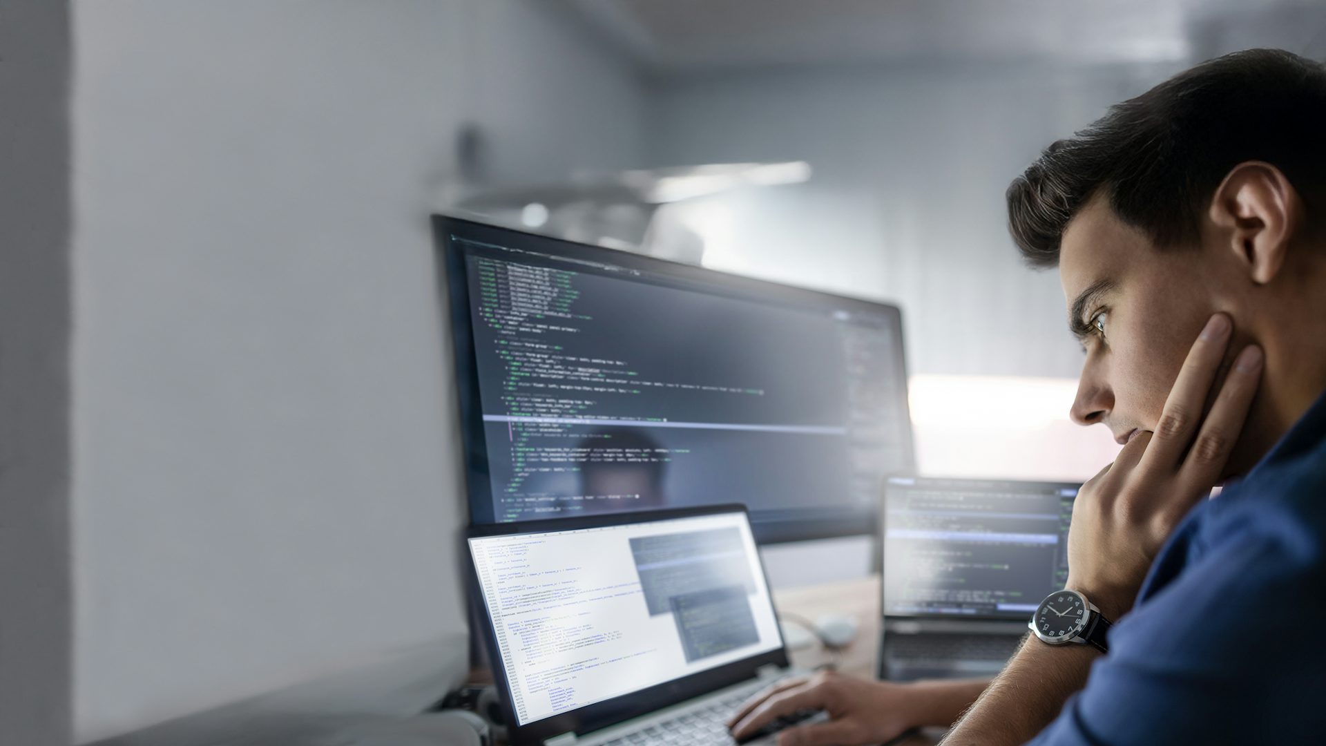 Programmer works on a laptop with multiple screens in a company office.