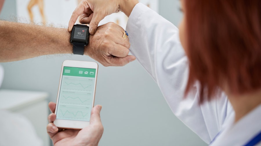 A doctor looking at a smart watch being worn by a patient who is holding up the data on a smart phone.