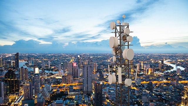 5G base station tower over city at sunset