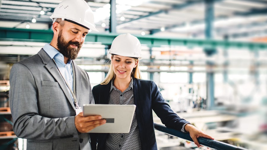 Zwei Hersteller überwachen die intelligente Fabrikhalle und betrachten ihr Manufacturing Execution System auf einem Tablet.