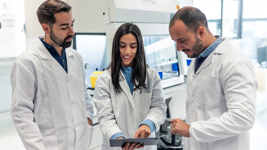 A team of three medical device colleagues looking a tablet in a lab.
