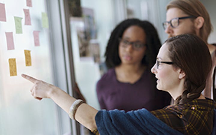 Drei Personen betrachten Klebezettel an einem Whiteboard
