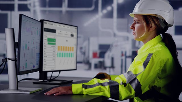 Engineer operator sitting at desk and using desktop computer at an industrial plant.