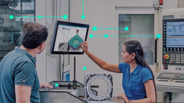 A man and woman in a shopfloor setting reviewing a part using NX CAM software. 