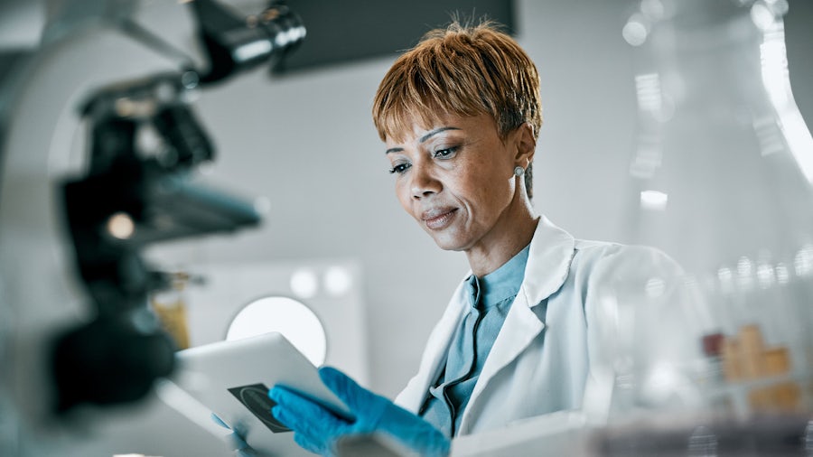 Eine Frau in einem weißen Laborkittel in einem Labor schaut auf ein Tablet.