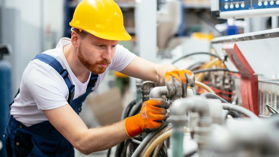 A service engineer works to repair an industrial machine on the factory floor.