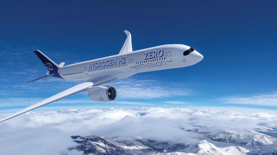 A white airplane with the words “Hydrogen H2 zero emissions” printed on it flies above the clouds with a bright blue sky in the background