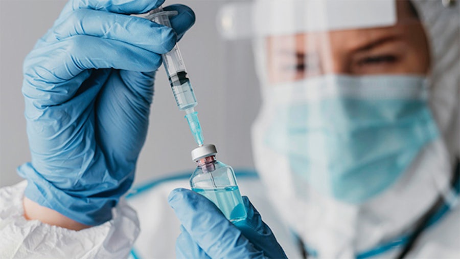 Healthcare provider in a mask and face shield using a syringe to extract liquid from a vile. 