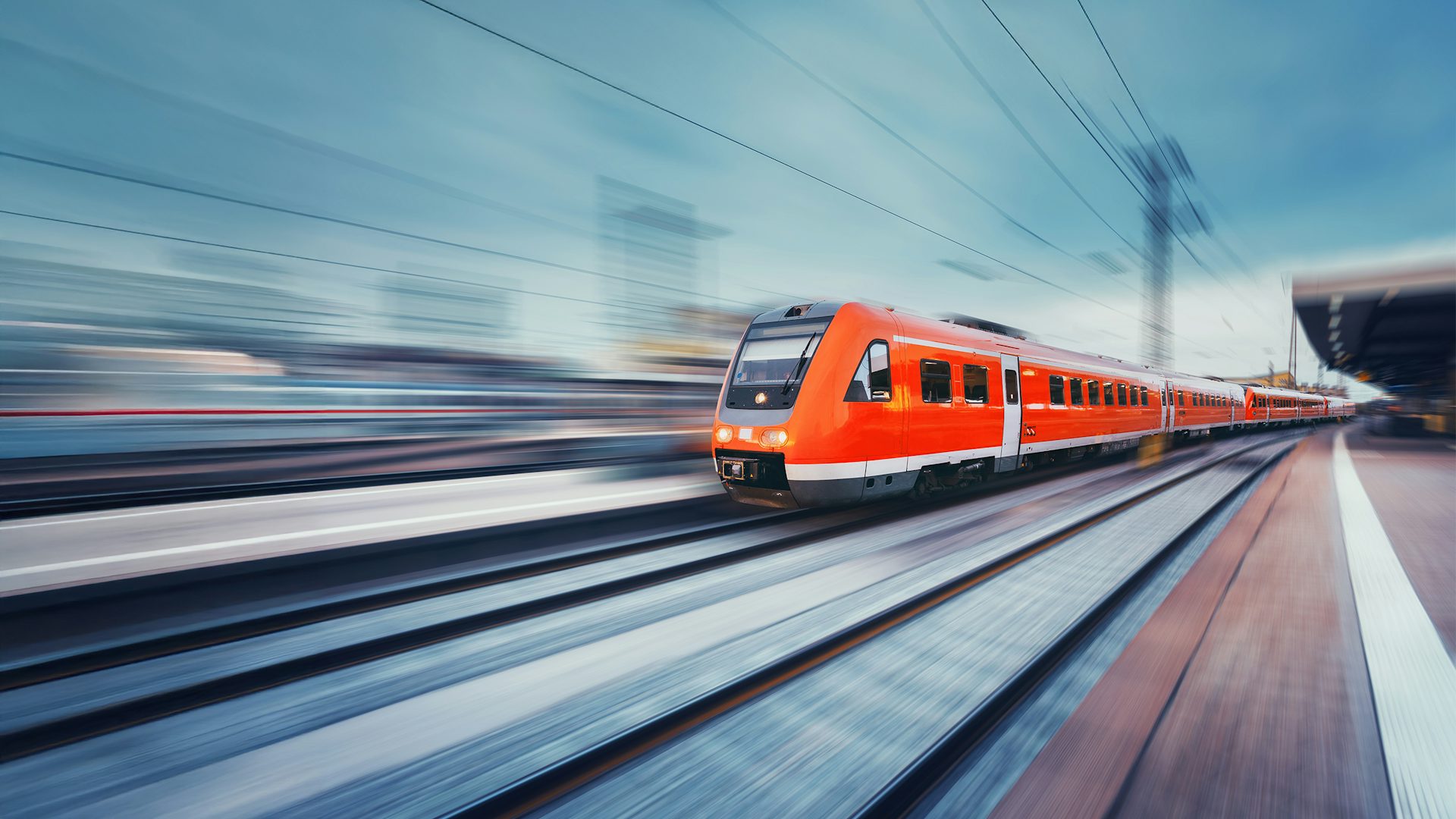 Modern red high-speed commuter train moving along a railway platform.