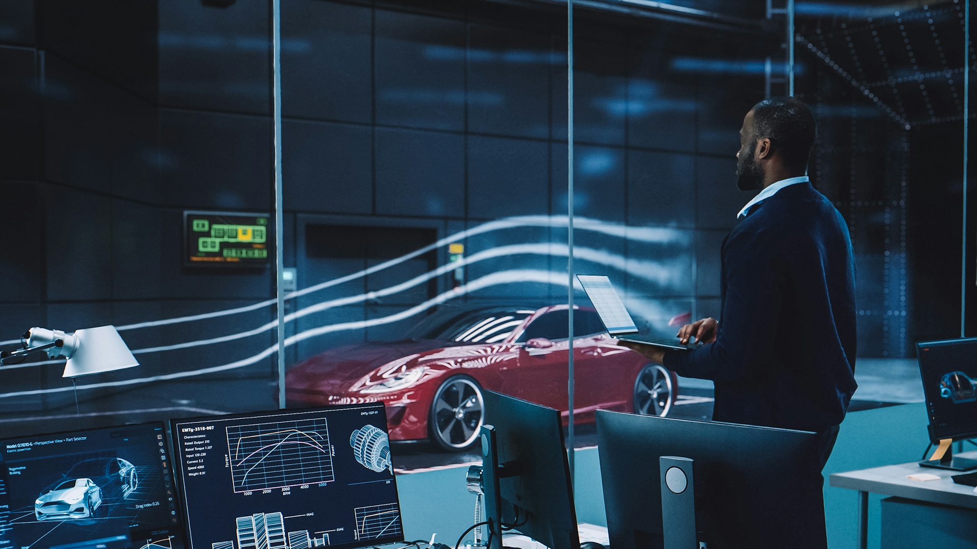 Engineering research agency performs testing with an electric sports car in a wind tunnel. Professional works on a laptop changing testing options.
