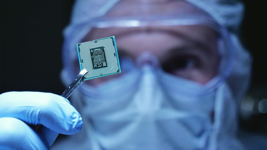 Man in inspecting semiconductor chip in clean room.