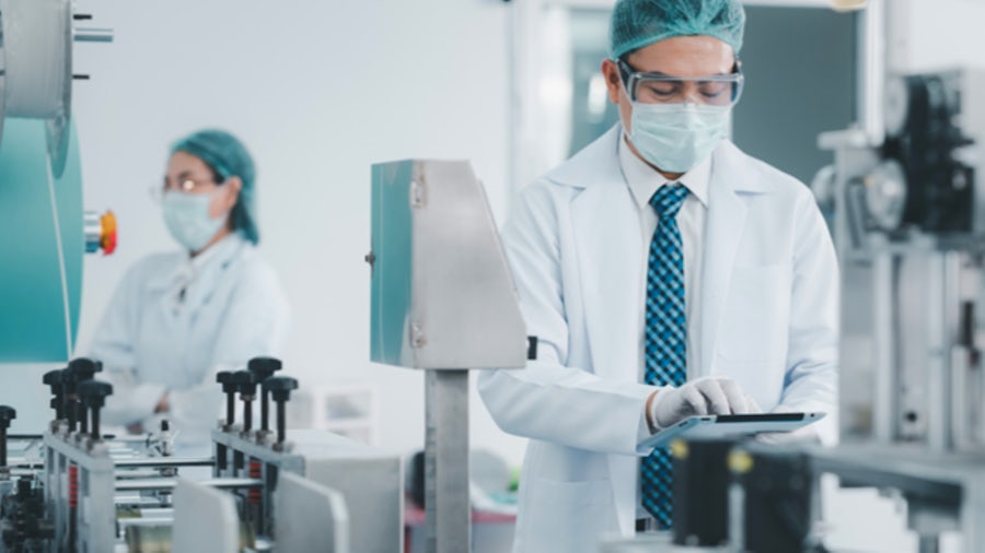 Male in PPE holding tablet in a medical device lab