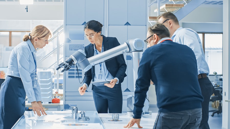 Industrial Robotics Engineers Gathered Around Table With Robot Arm