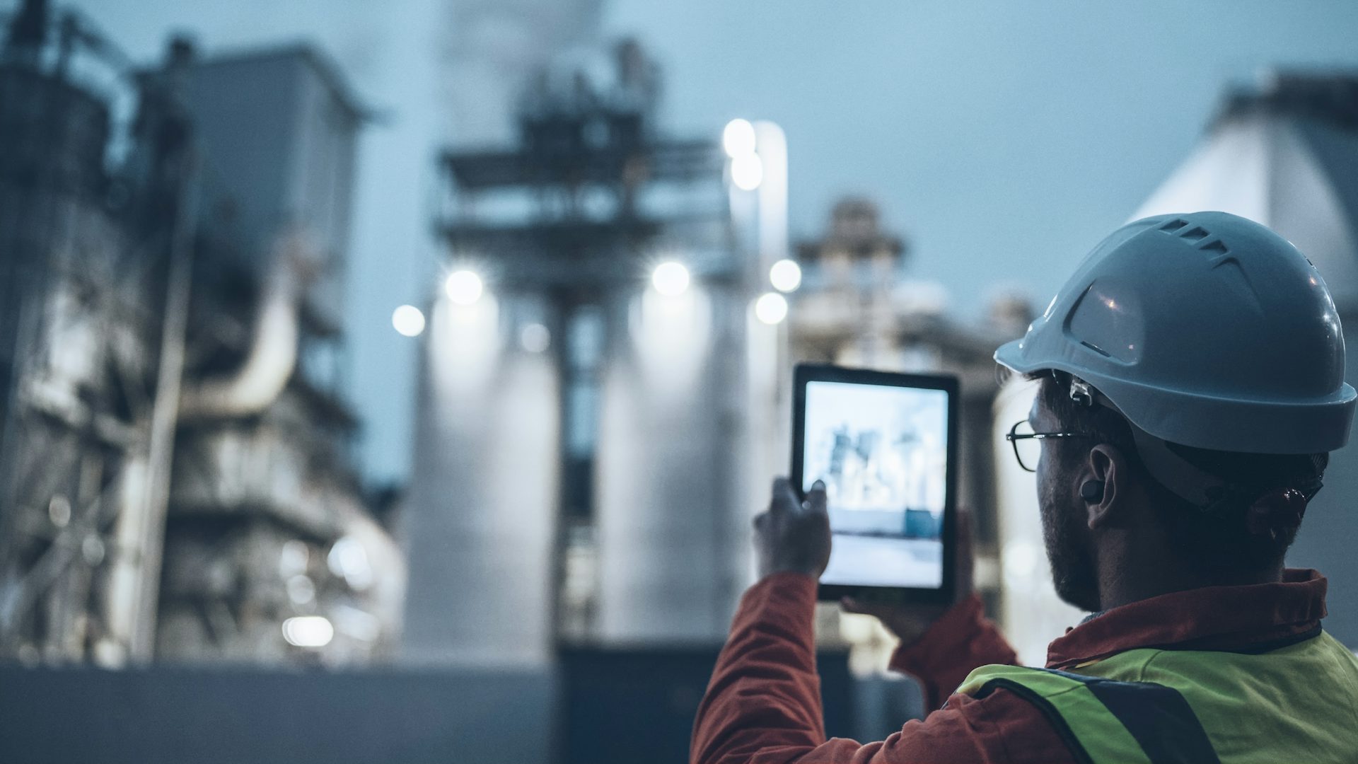 Close-up of engineer in front of process plant at dusk holding up a tablet