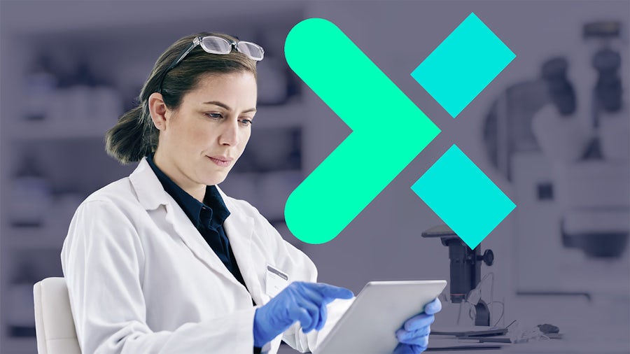 A brunette woman with reading glasses perched on her head looks at a tablet while wearing blue protective gloves.