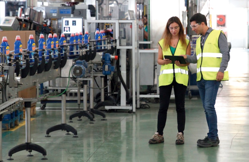 Trabajadores de una fábrica mirando una tablet cerca de la línea de producción de detergente.