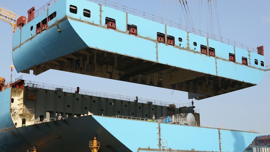 A large crane lowers a piece of a ship under construction into place 