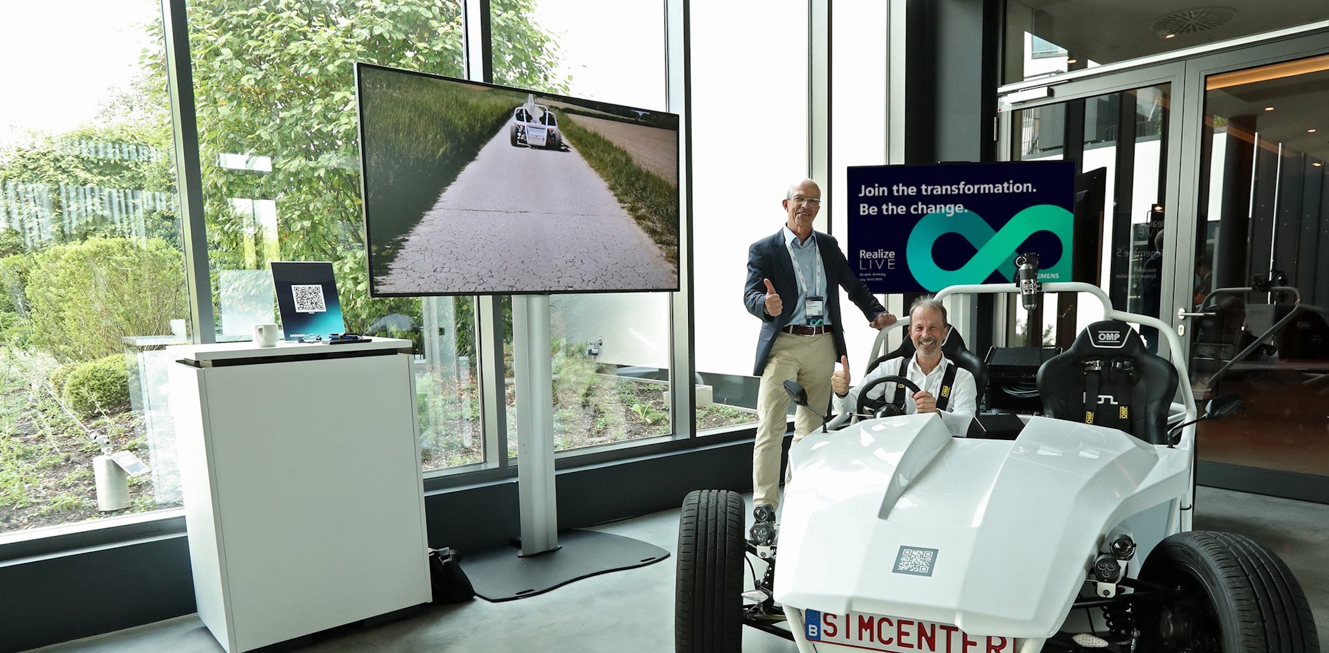 A Siemens exhibit presenter looks on, as a Realize LIVE attendee participates in a demo of a car and Simcenter software,