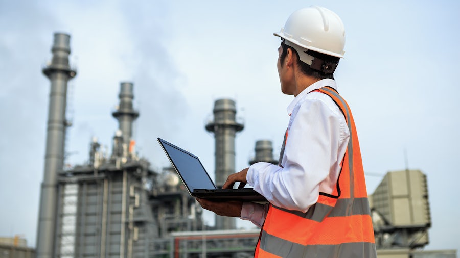 Engineer with laptop computer in front of refinery