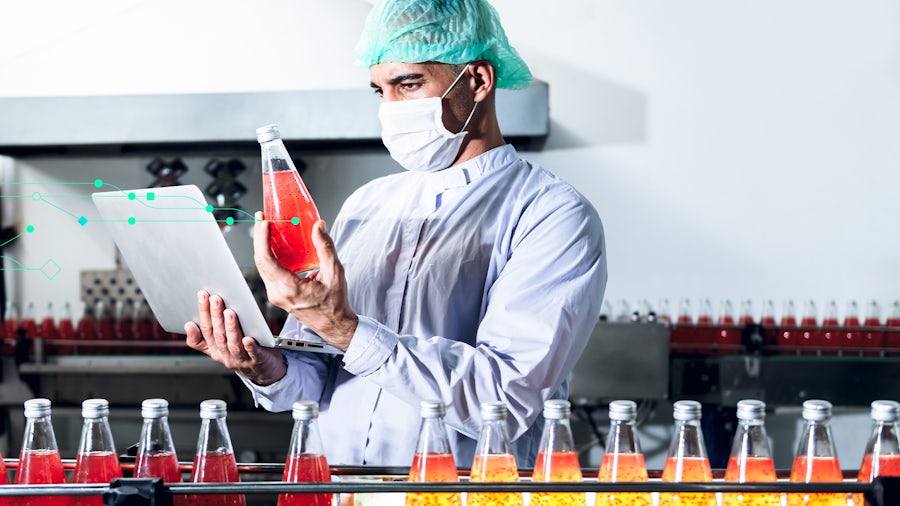 Person working in bottling factory holding a bottle and looking at a computer screen 