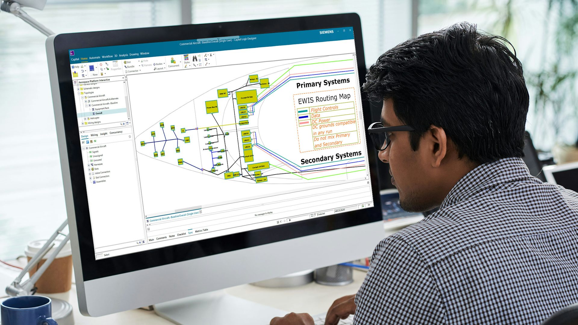 A man sits at a desk looking at the topology of an aircraft on a computer screen in an office setting. The screen displays various metrics.