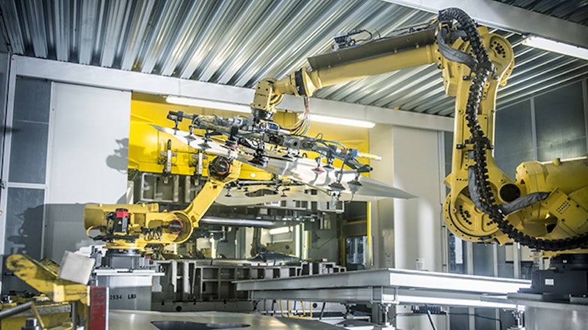 Žlutý robot pracující s průmyslovými stroji v továrně.