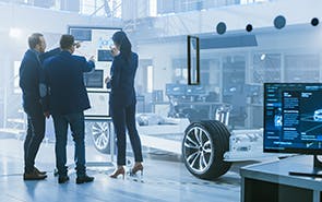 In a manufacturing environment, engineers discuss automotive components that are presented on a vertical display.
