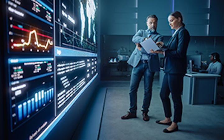 Zwei Geschäftsleute vor einem leuchtenden Display mit Laptop in der Hand.