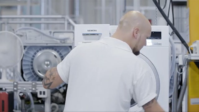 Uomo con una maglietta bianca che assembla un'asciugatrice a marchio Siemens.