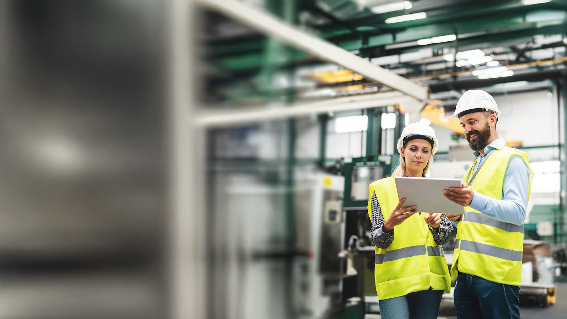 Industrial man and woman engineers talking while working on a tablet in a factory.