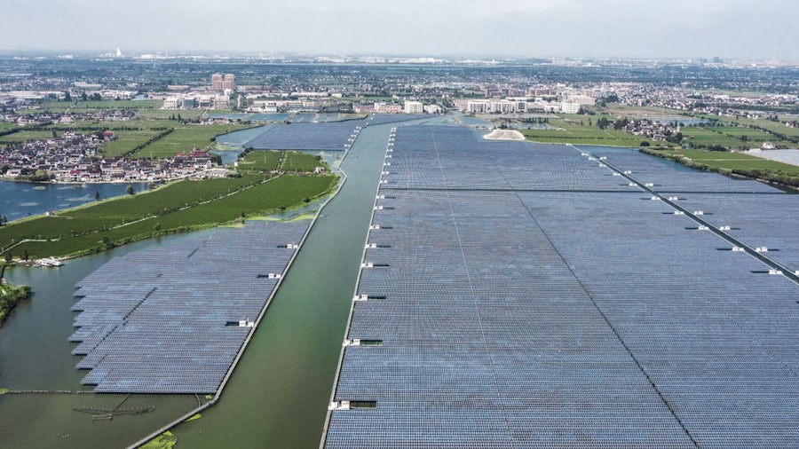 Una gran granja de paneles solares utiliza energía solar para suministrar electricidad a una ciudad en el fondo.