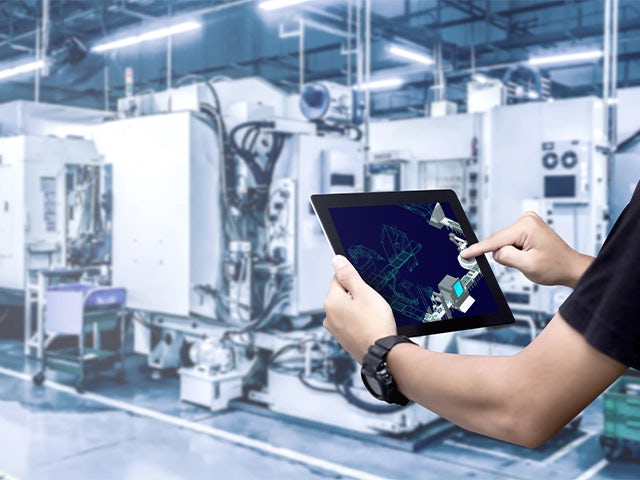 A man holding a tablet with a plant simulation on the screen while standing in a medical device manufacturing facility.
