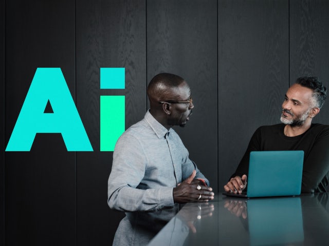 Two men collaborating while working on a laptop with the Siemens AI shape beside them.
