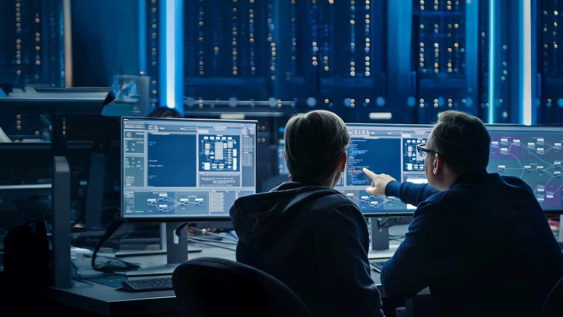 Two IT professionals discussing work displayed on a computer monitor in a data center with server racks.