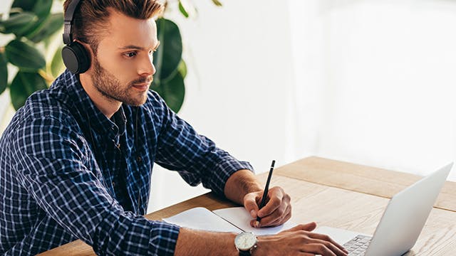 side view of man in headphones watching a webinar with notebook in office